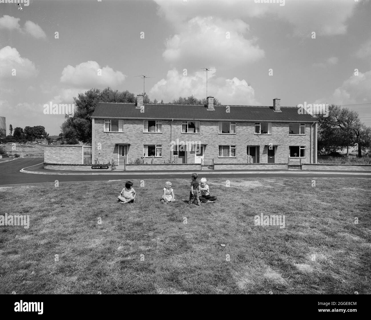 Eine Gruppe von Kindern, die auf dem Gras vor einer Reihe von Easiform-Reihenhäusern auf Sundaw Close spielen. „Easiform“ war eine Methode der in situ vorgegossenen Betonkonstruktion, die John Laing und Son Ltd ab 1919 entwickelten. Stockfoto