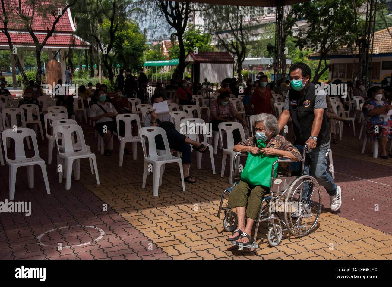 Ein Gesundheitsmitarbeiter schiebt einen Rollstuhl für eine ältere Frau an der Raj Pracha High School in Samut Prakarn.das Bang Chak Hospital in der Provinz Samut Prakarn wurde für die Einwalk-Impfung der Einwohner von Samut Prakarn eröffnet, um ihre erste Dosis des Pfizer-Impfstoffs am Raj Pracha High zu erhalten. Einwohner der Provinz Samut Prakarn mit hohem Risiko, die sich für den Impfstoff qualifiziert haben, sind über 60 Jahre alt, schwanger, Oder haben bereits bestehende Erkrankungen ihre erste Dosis des Pfizer-BioNTech COVID-19-Impfstoffs erhalten, die zwischen dem 30. August und dem 1. September 2021 um 8:00 Uhr und 14:00 Uhr begann (Foto: Peerapon Boonyakiat/SOPA Images/Si Stockfoto