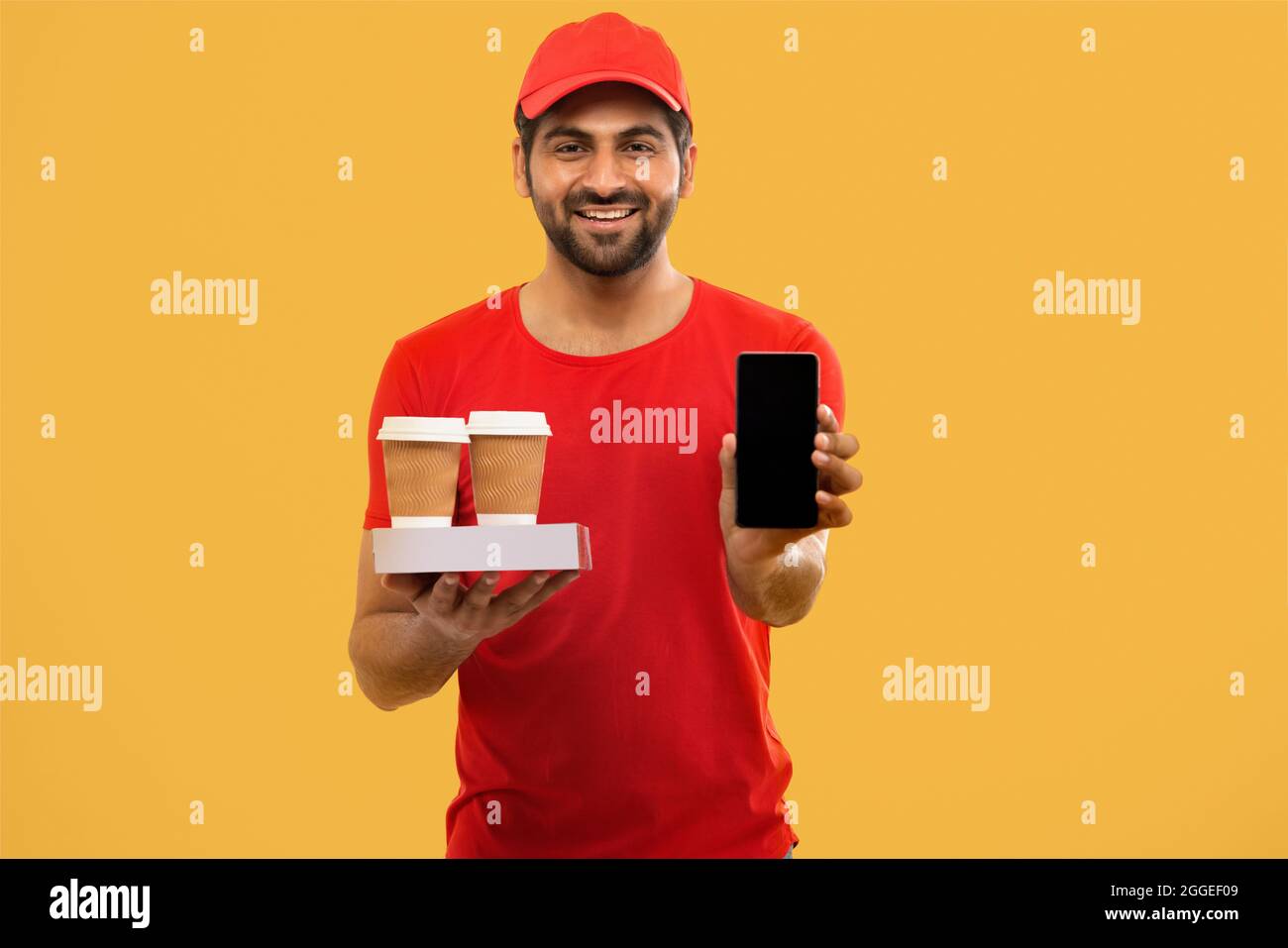 EIN LIEFERER, DER MIT VERPACKTEN LEBENSMITTELN STAND UND DAS HANDY ZEIGTE Stockfoto