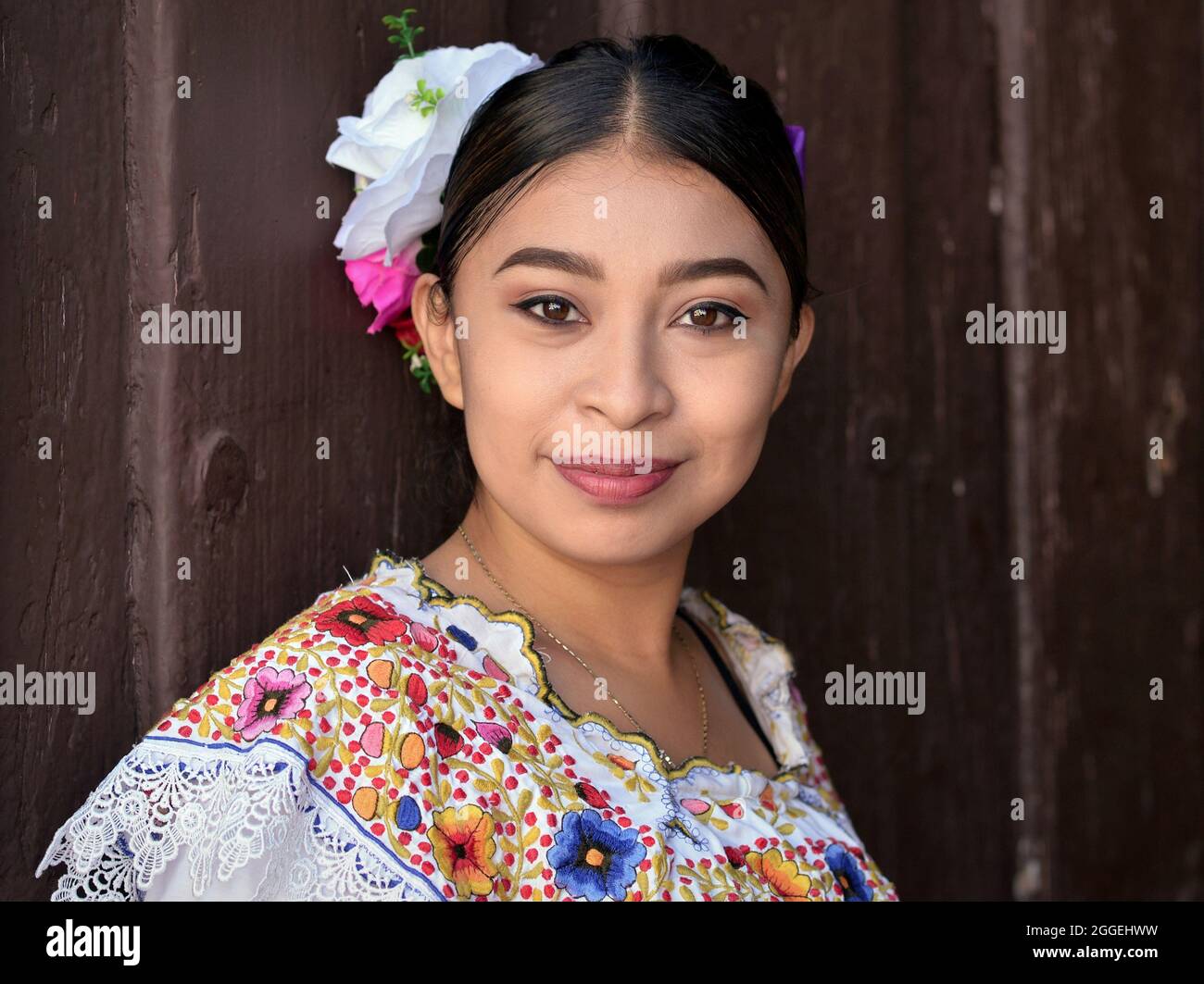 Junge schöne mexikanische Frau mit Make-up trägt traditionelles Maya Yucatecan folklorisches Kleid mit Blumen im Haar und posiert für die Kamera. Stockfoto