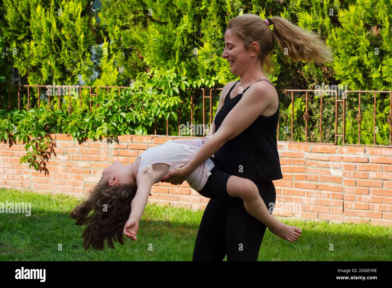 Die junge Frau tanzt im Garten mit ihrer kleinen Tochter in den Armen. Selektiver Fokus. Film. Stockfoto
