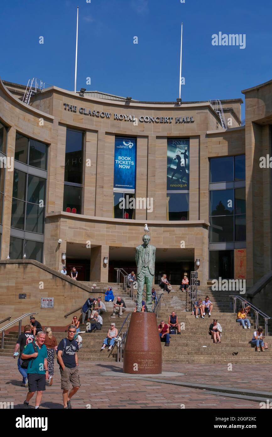 Die Menschen genießen den Sonnenschein auf den Stufen hinter der Donald Dewar-Statue vor der Royal Concert Hall, Buchanan Street, Glasgow City Centre, Schottland, UK Stockfoto