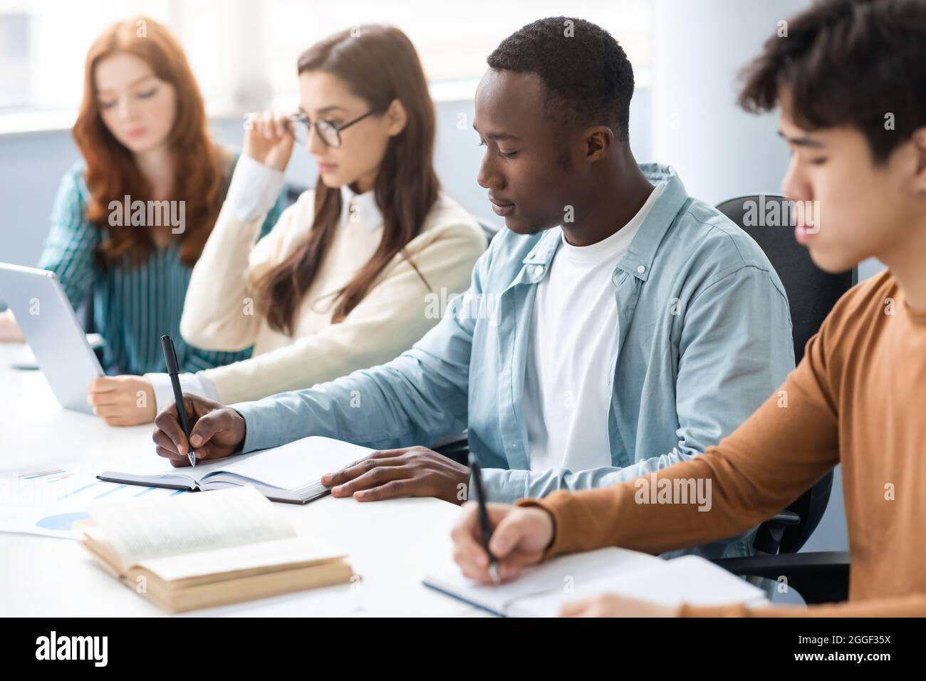 Lernprozesskonzept. Porträt diverser Studenten, die am Schreibtisch sitzen und sich Notizen machen und gemeinsam an Einem Gruppenprojekt arbeiten. Internationale Sie Stockfoto