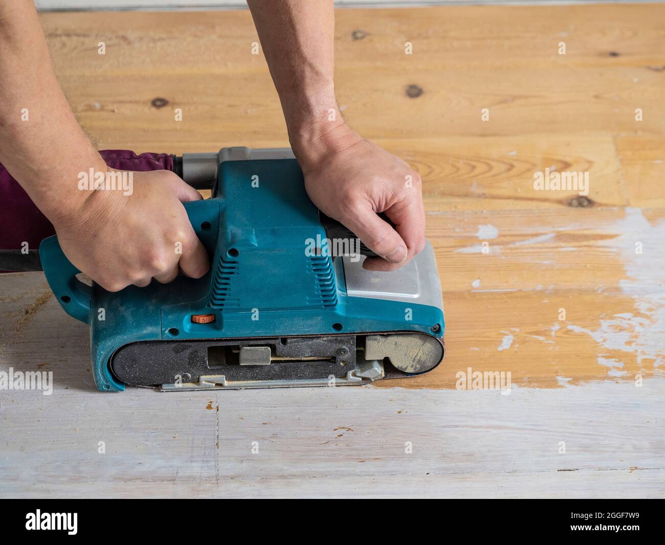 Nahaufnahme von kaukasischen männlichen Händen, die einen Bandschleifer bedienen, um weiße Farbe von einem Holzboden zu entfernen. Stockfoto