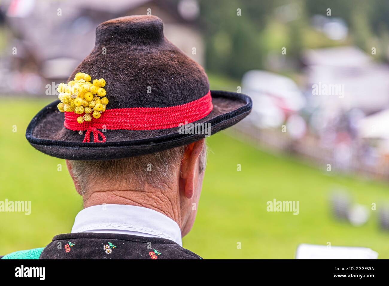 Der schwarze traditionelle Hut eines Alphornspielers, mit einem roten Band und gelber Blumendekoration, hebt sich vor einem grünen Hintergrund an der Gompm-Alm beim Gourmet-Event "Unplugged Taste" in Südtirol, Italien ab; Alphörner gehören zum herzhaften Folklore der Region. Stockfoto