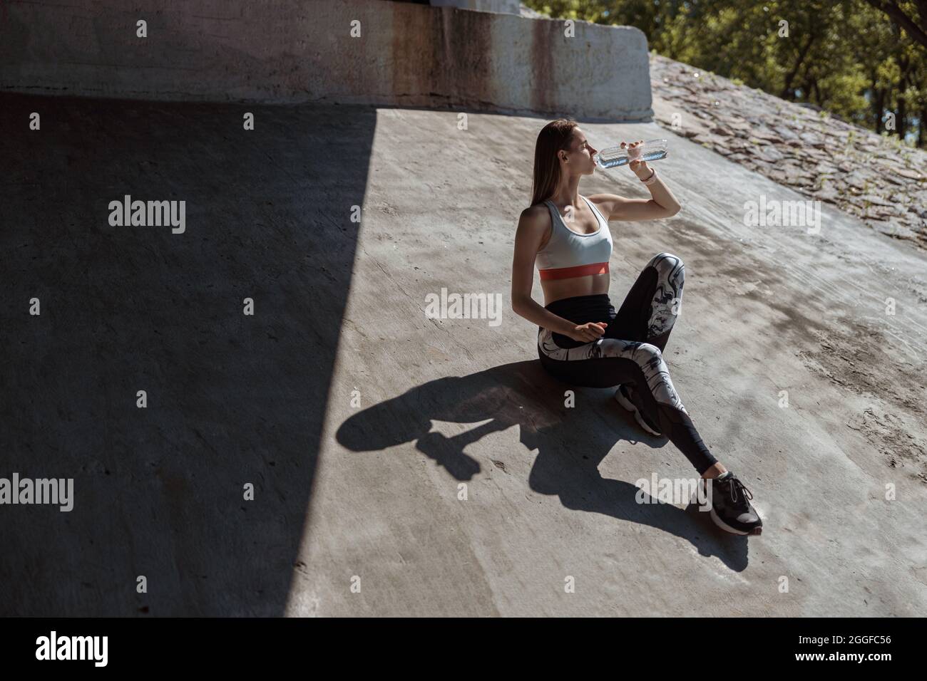 Attraktive Frau im Trainingsanzug trinkt Wasser auf Betonboden Stockfoto
