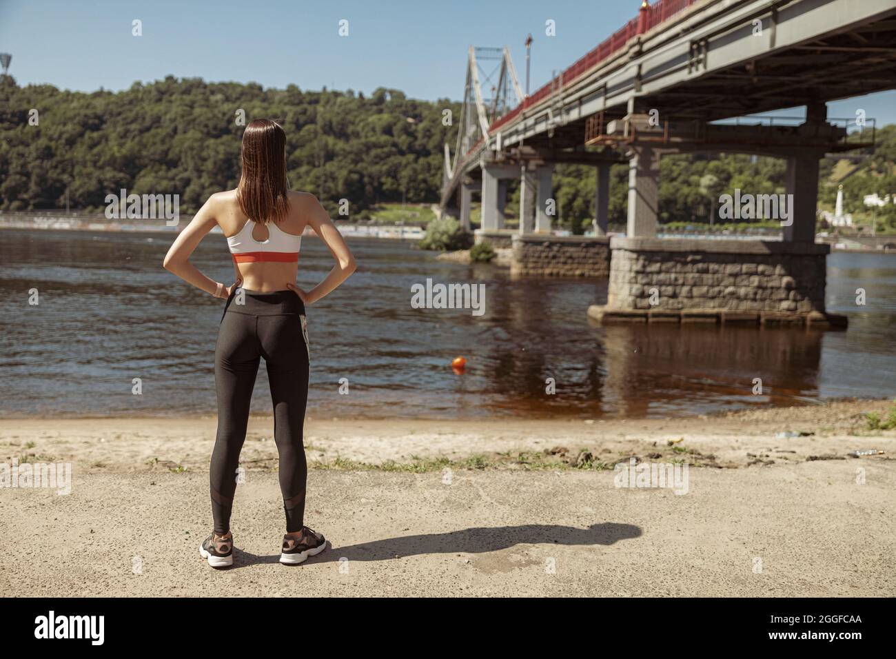 Frau in Sportkleidung blickt auf den Fluss, der auf einer Sandbank steht Stockfoto