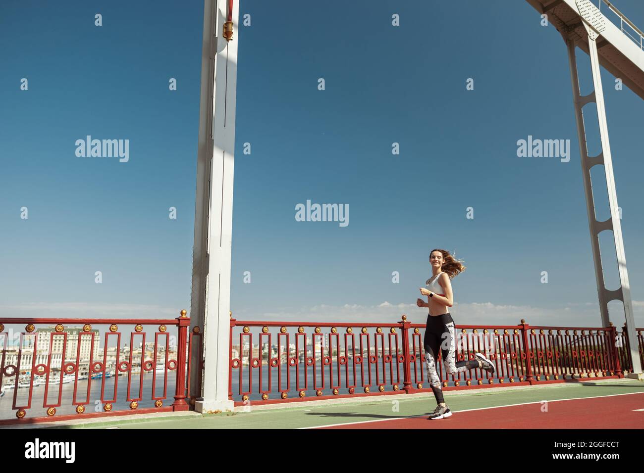 Lady mit fliegenden Haaren waering stilvoller Trainingsanzug läuft entlang des modernen Steges Stockfoto