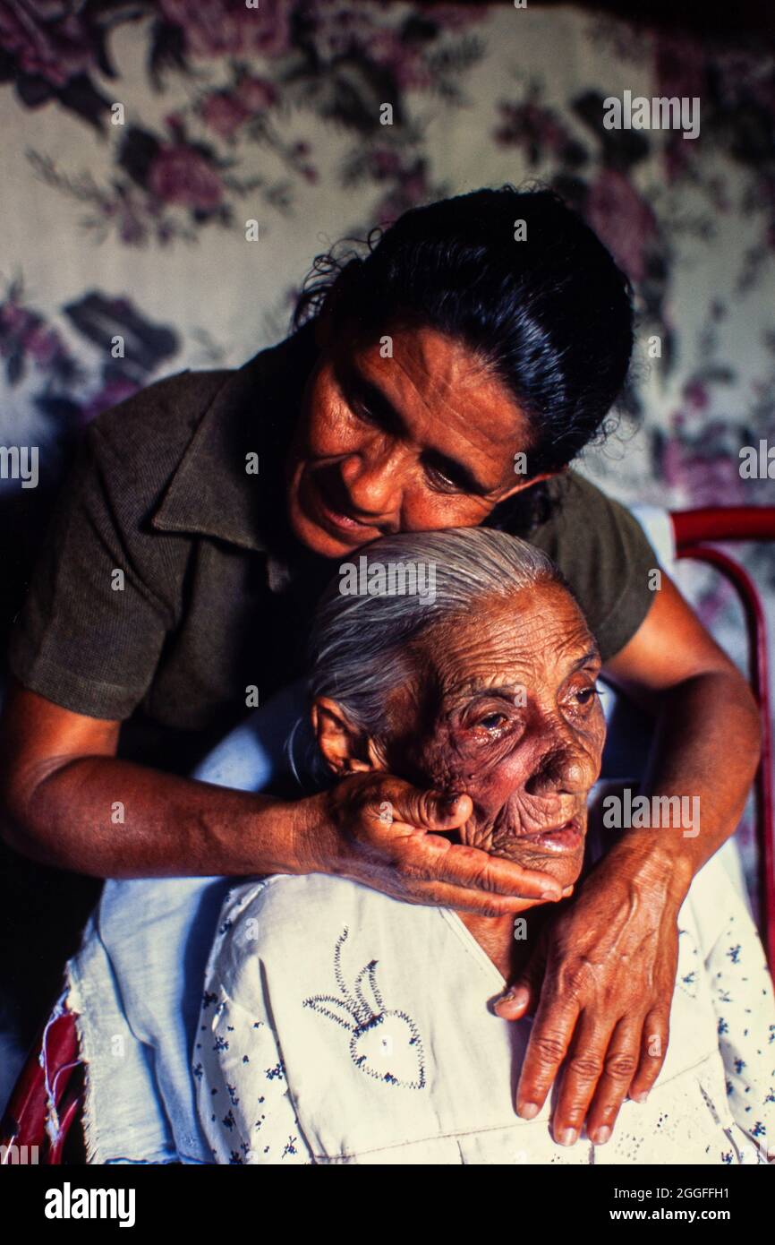Frau mittleren Alters tröstet ihre ältere, behinderte Mutter im Bett. Stockfoto