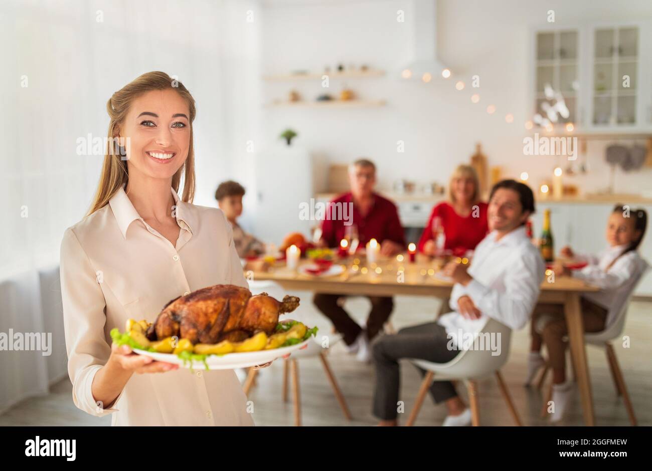 Glückliche junge Frau hält gebratenen truthahn zu Thanksgiving oder Weihnachten, Serviertisch für die große Familie, feiert traditionelle Feiertage mit ihrer Nahe ein Stockfoto