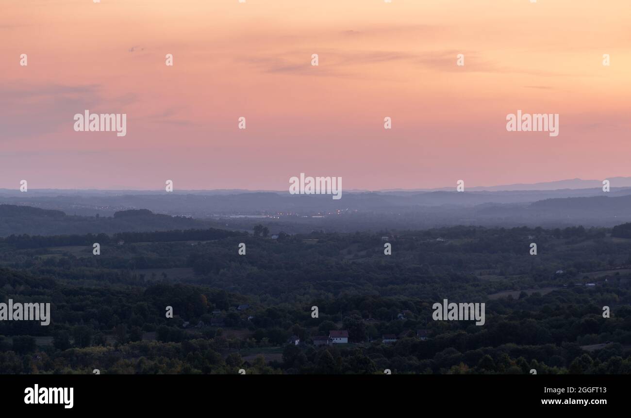 Landschaft mit Wäldern und Wiesen in Dunst und lila Farbe am Himmel in der Dämmerung Stockfoto