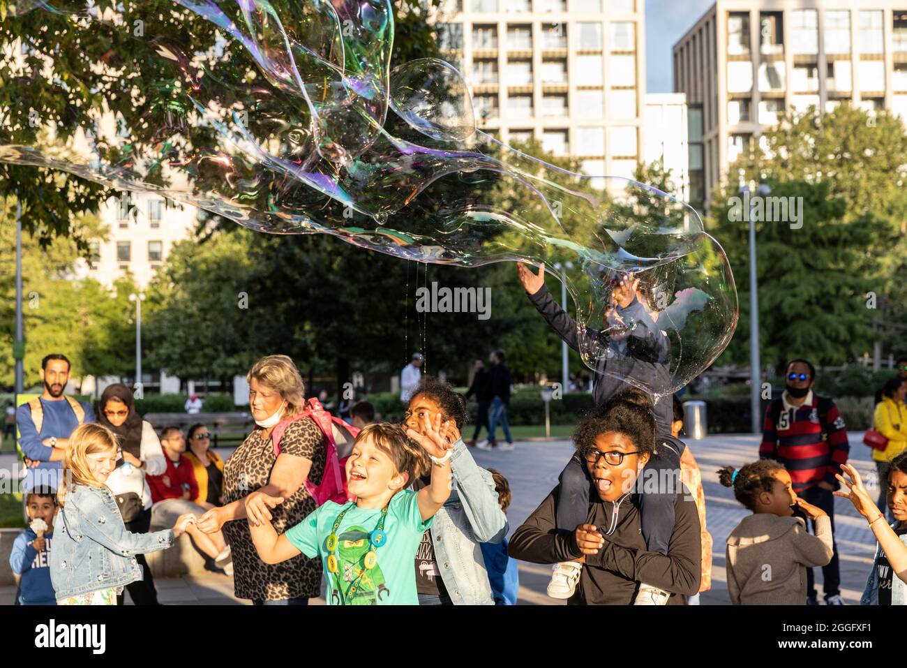 Familien genießen die Straßenunterhaltung entlang der Southbank in London, während ein Darsteller große Blasen über den Bürgersteig bläst, England, Vereinigtes Königreich. Stockfoto