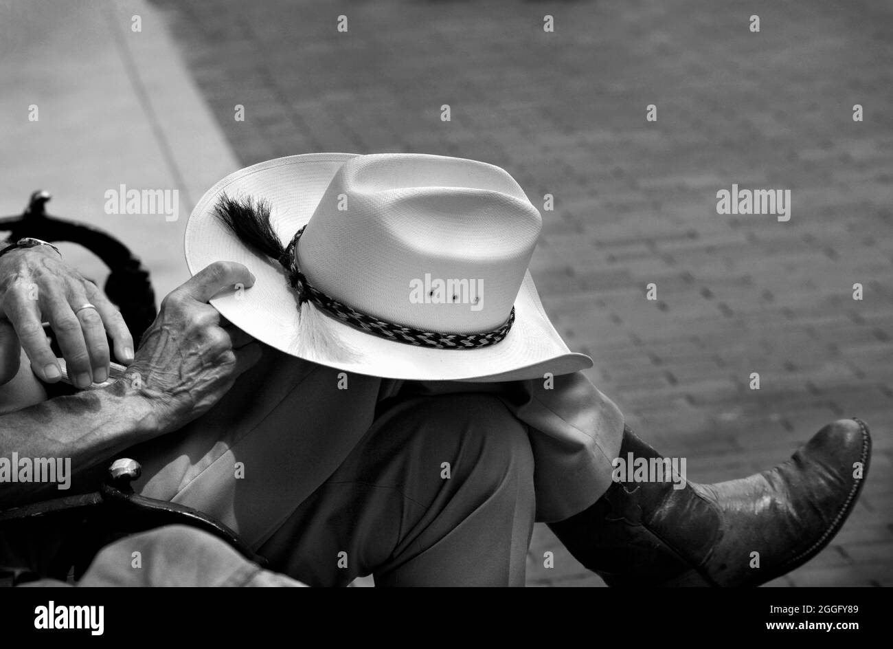 In Santa Fe, New Mexico, sitzt ein Mann in westlicher Kleidung auf einer Parkbank mit seinem Hut auf dem Knie. Stockfoto