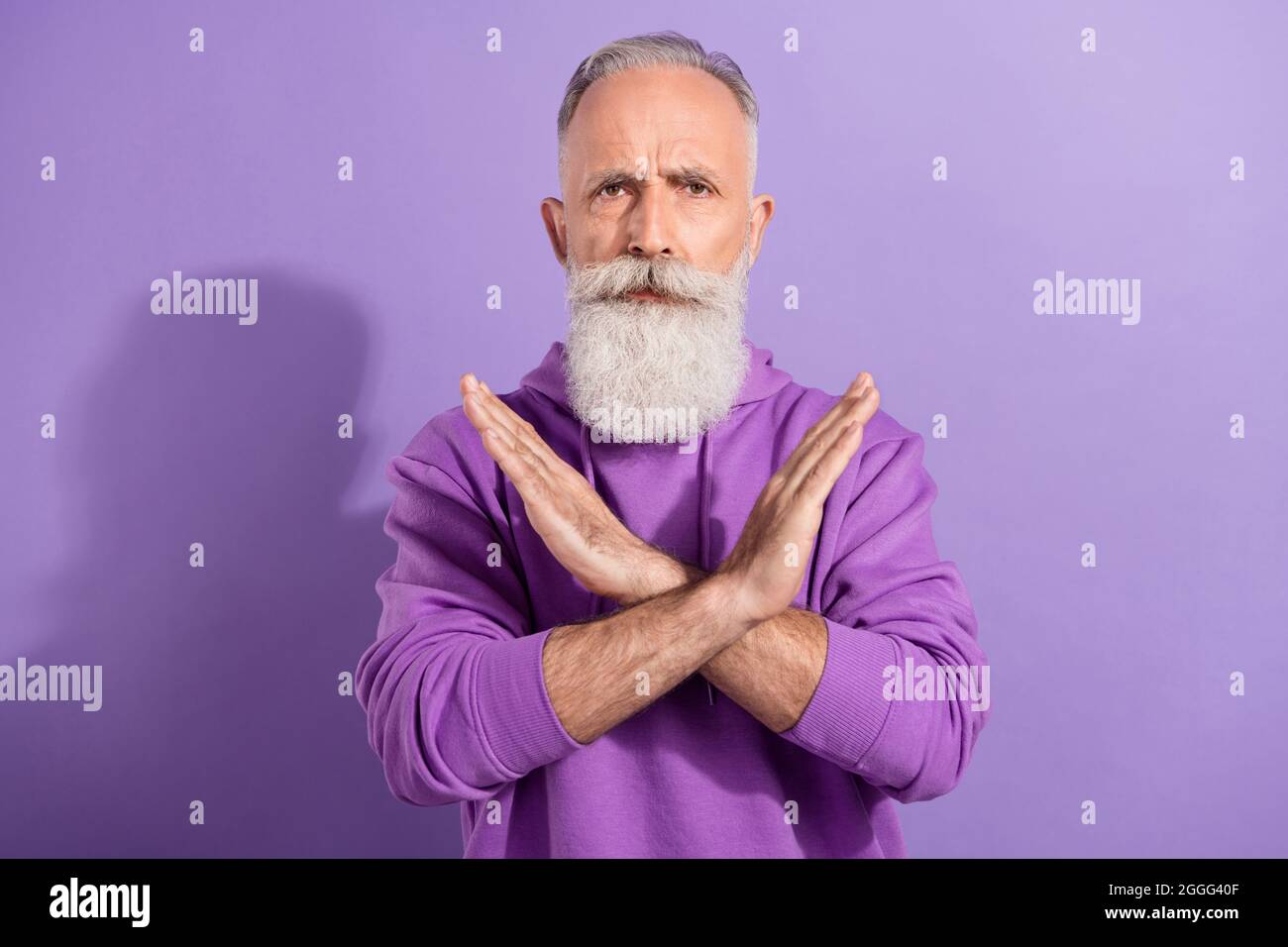 Porträt eines älteren Rentners grauhaarige Kapuzenjacke mit gekreuzten Händen, isoliert auf violettem Hintergrund Stockfoto