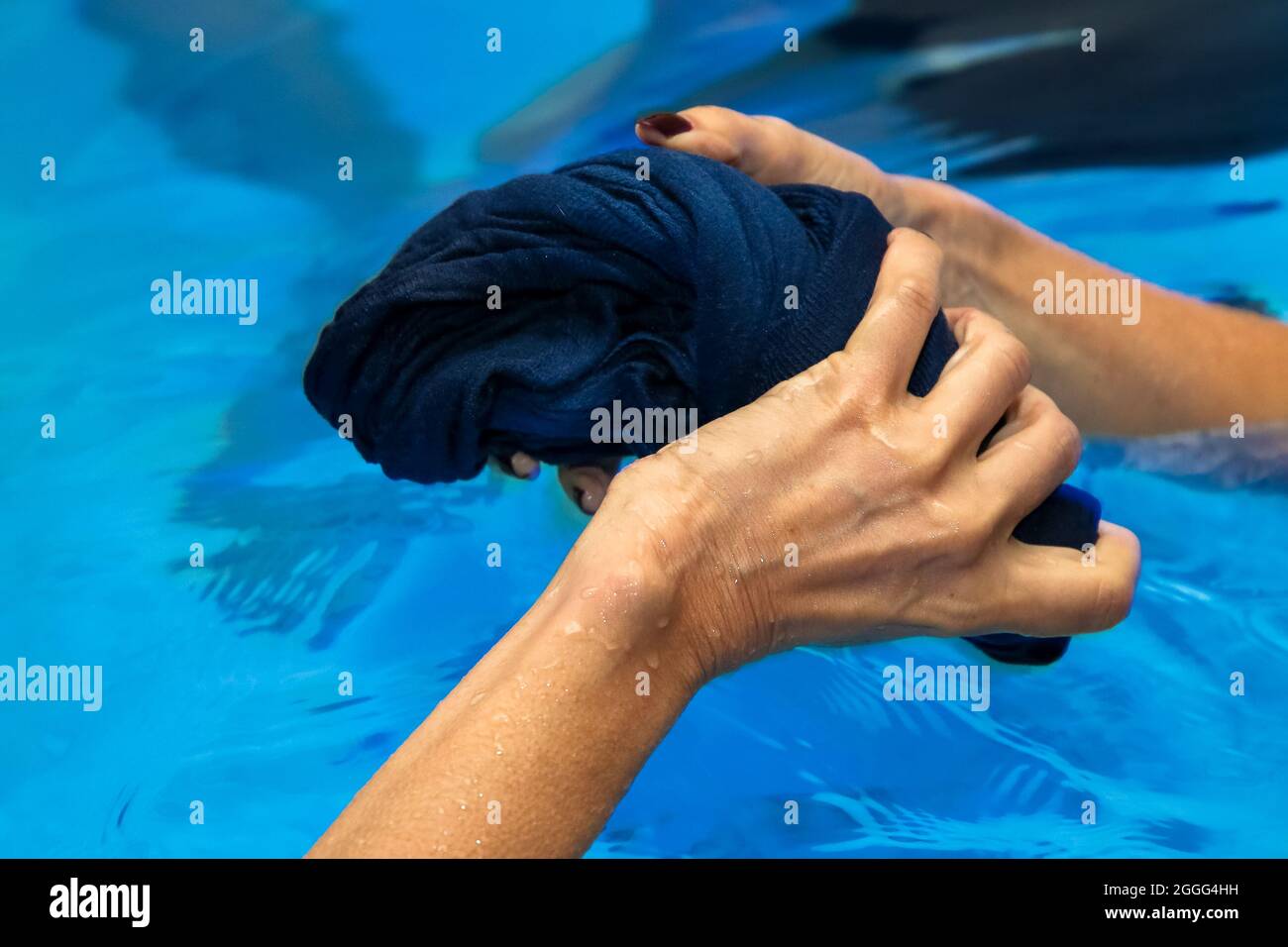 Nahaufnahme der Hände einer Frau in einem Pool, die ein nasses Hemd quetschen Stockfoto