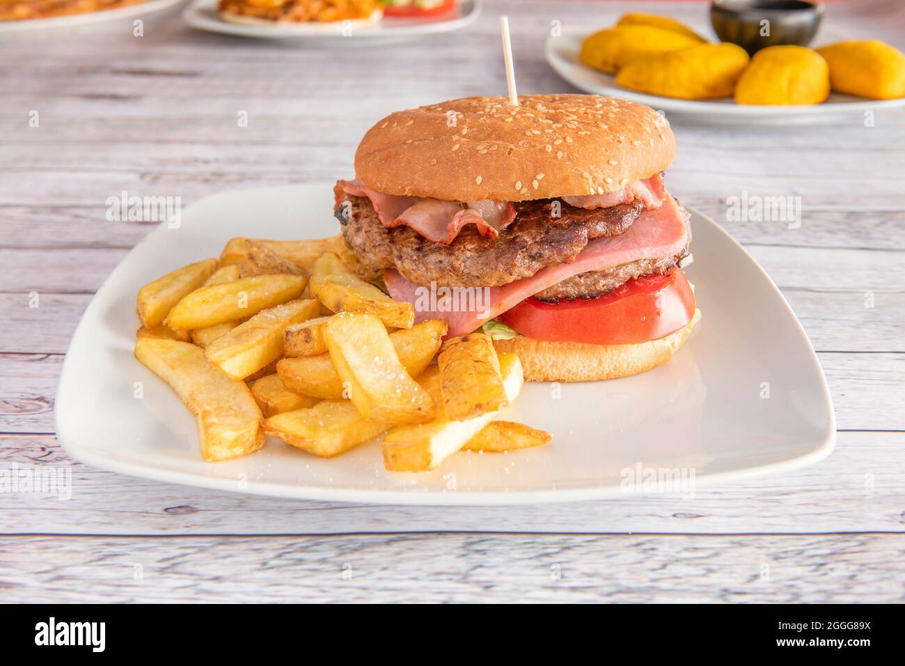 Klassischer Hamburger mit zwei Fleischsorten, Schinken, Bank, Tomatenscheiben und Pommes frites Stockfoto