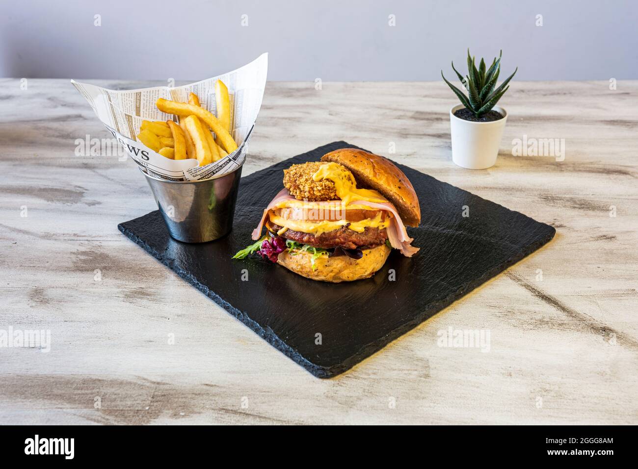 Rinderburger mit Cheddar-Käse und Nuggets, gebratenem Speck und Salat, garniert mit Pommes auf Holztisch Stockfoto