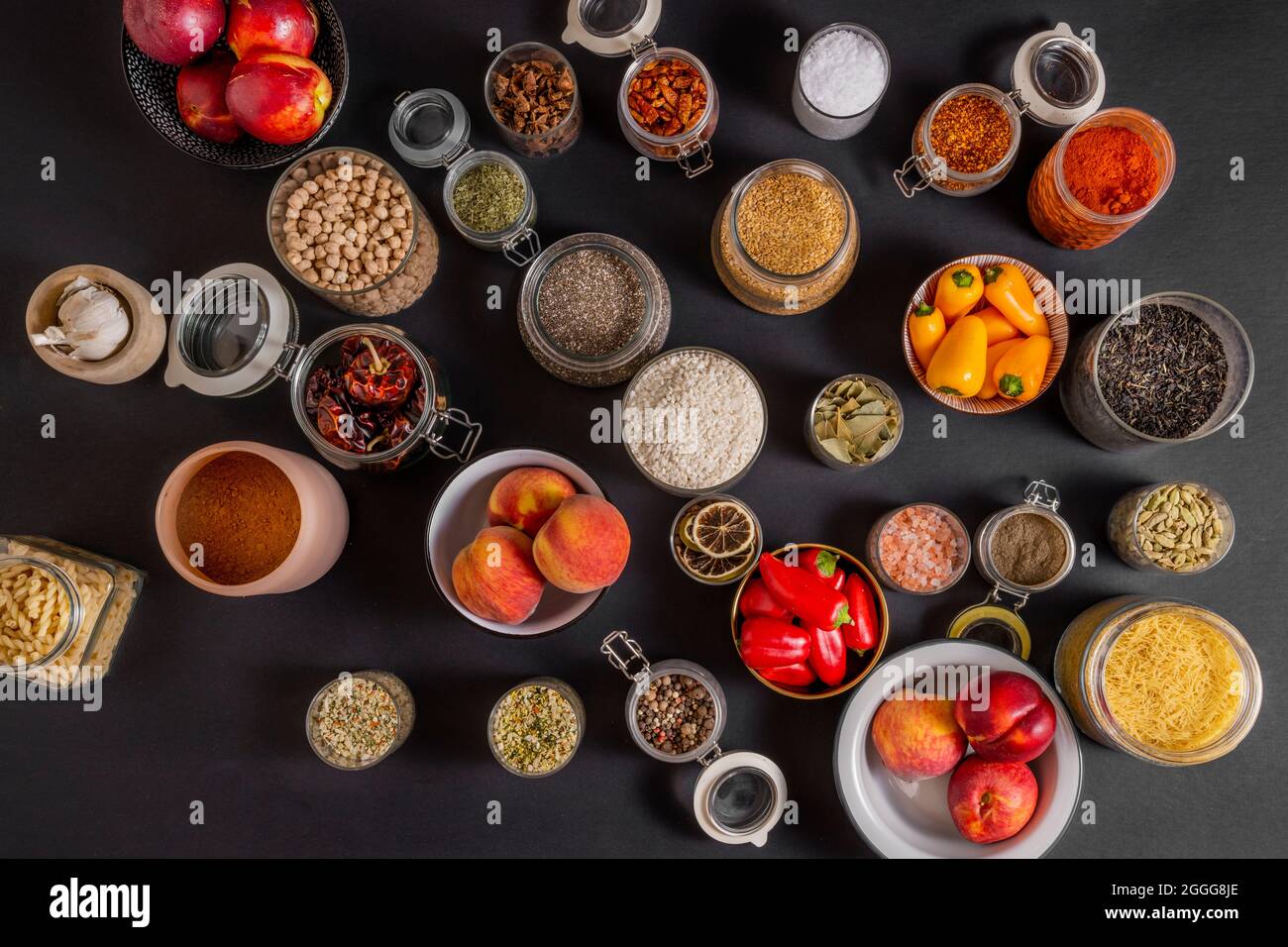 Draufsicht auf viele Glasgefäße, gefüllt mit allerlei Gewürzen und Früchten auf schwarzem Hintergrund Stockfoto
