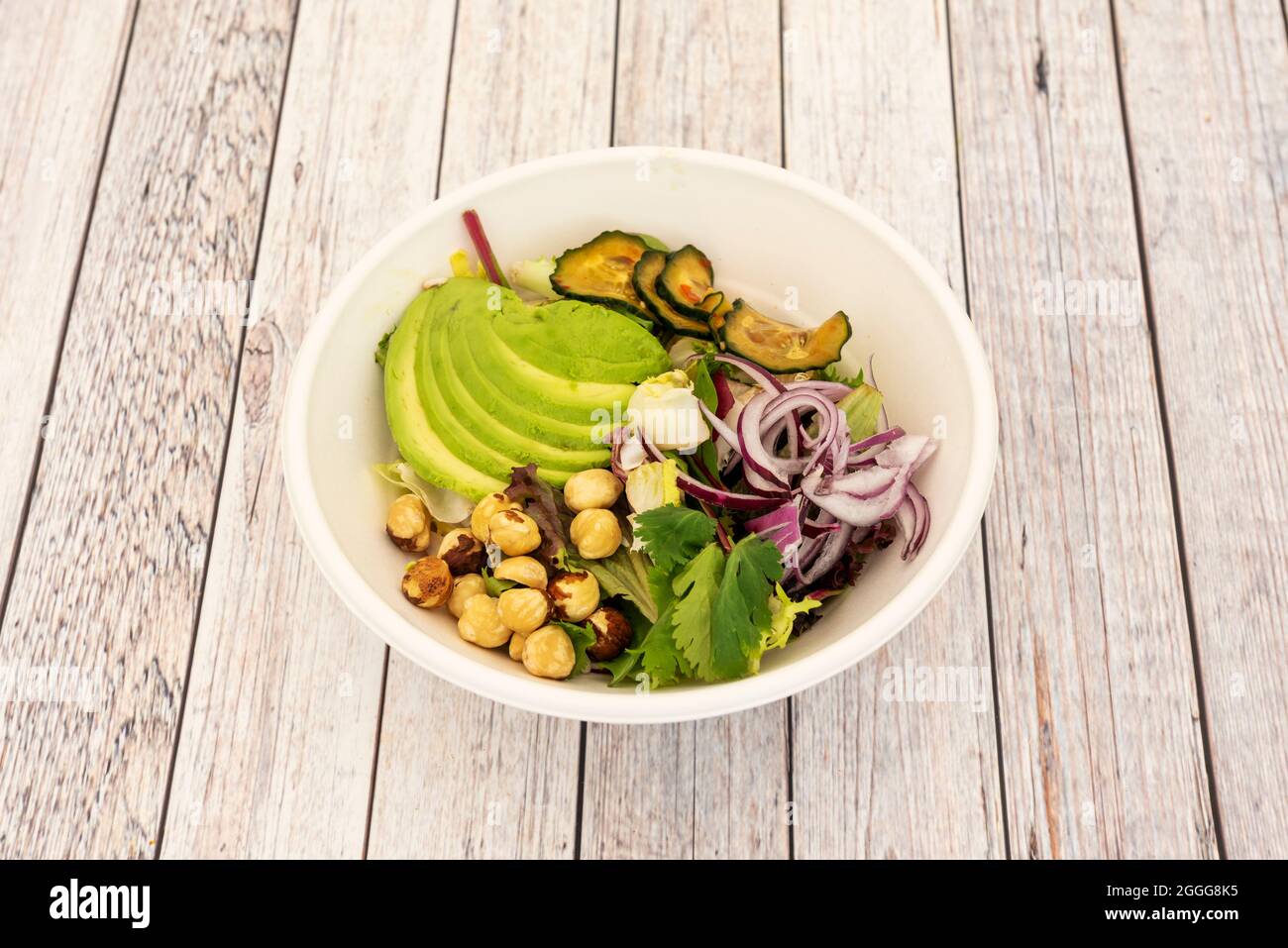 Gemüsesalat mit Koriander, gehackter reifer Avocado, roter Zwiebel, gerösteten Gurken, ganzen Haselnüssen und Salatsprossen in einer Schüssel für die Hauszulieferung Stockfoto