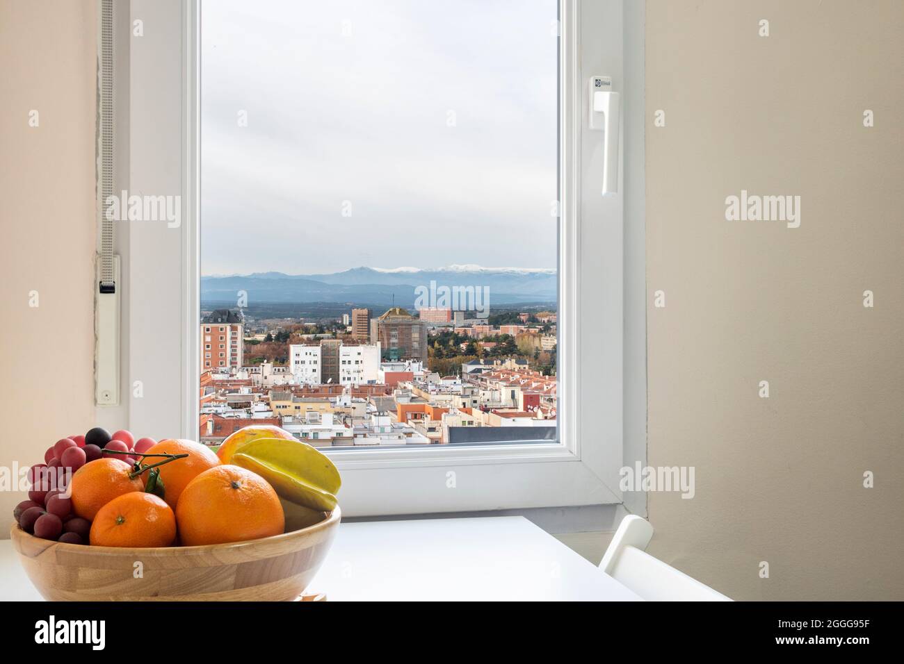 Volle Obstschale und Fenster mit Blick auf die Stadt und den verschneiten Berg Stockfoto