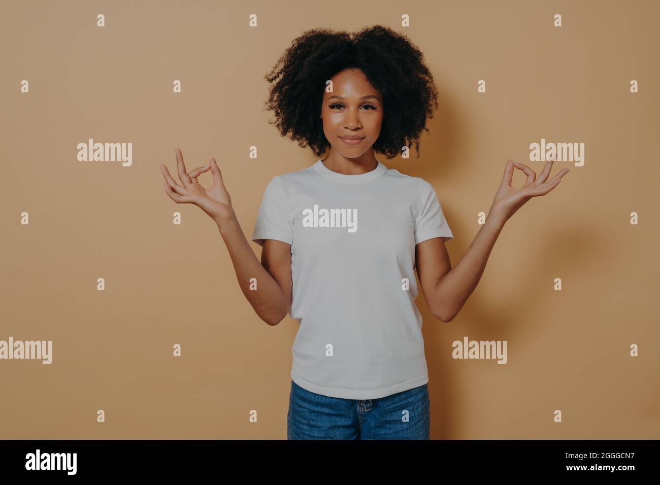 Friedliche afro amerikanische junge Frau, die die Hände in Mudra-Geste hält, isoliert auf beigefarbenen Wänden Stockfoto