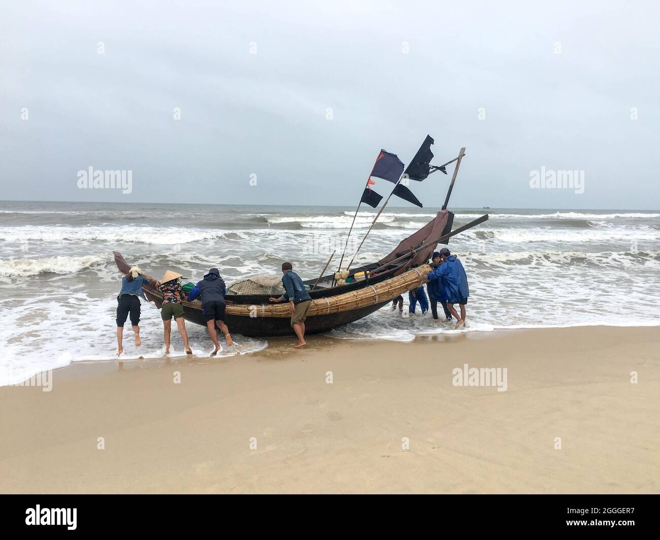 Quang Tri, Vietnam - 11. Februar 2020: Menschen schieben ein Fischerboot an einem windigen Tag am Strand der Provinz Quang Tri, Vietnam, ins Meer Stockfoto