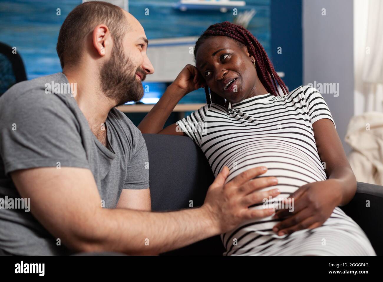 Fröhliche interracial Paar erwartet Baby zu Hause. Kaukasischer Ehemann und schwanger afroamerikanische Frau berühren Baby stoßen zusammen lächelnd. Multiethnische Menschen mit Schwangerschaft. Stockfoto