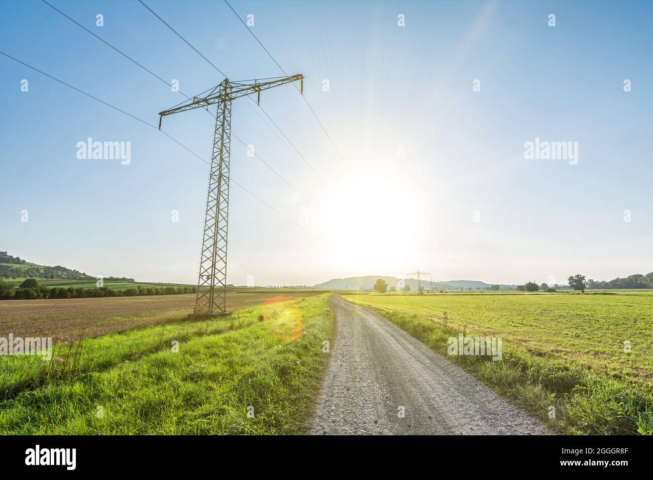 Stromleitung in ländlicher Landschaft mit landschaftlich reizvollen Sonnenstrahlen und Streulicht, die grüne, erneuerbare Energie symbolisieren Stockfoto