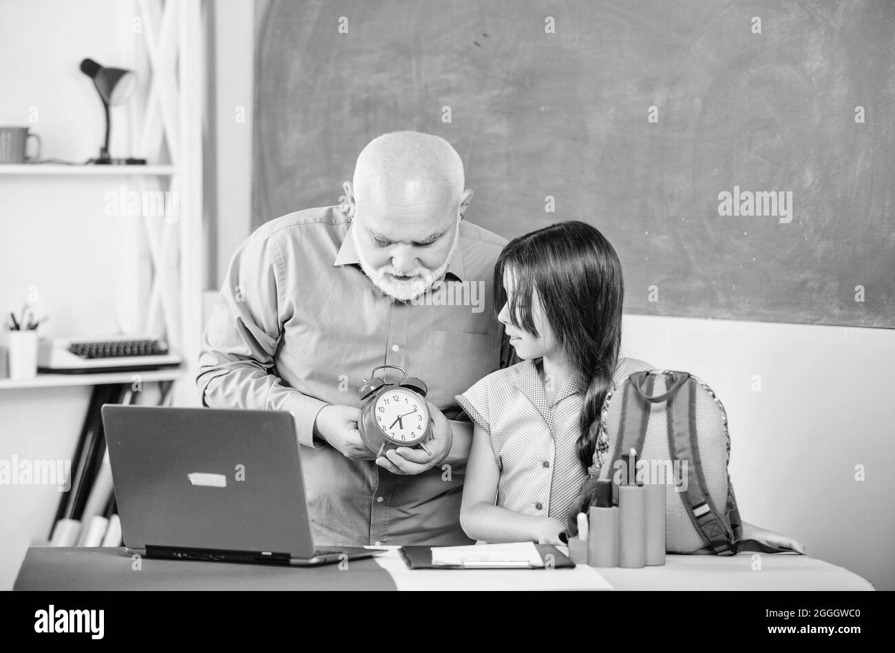 Kindererziehung. Reife Lehrer helfen Schüler mit Uhr. Kleines Mädchen mit Mann Tutor Studie am Computer. Break Alarm. Morgen. Zeit zum Lernen. Schule Stockfoto