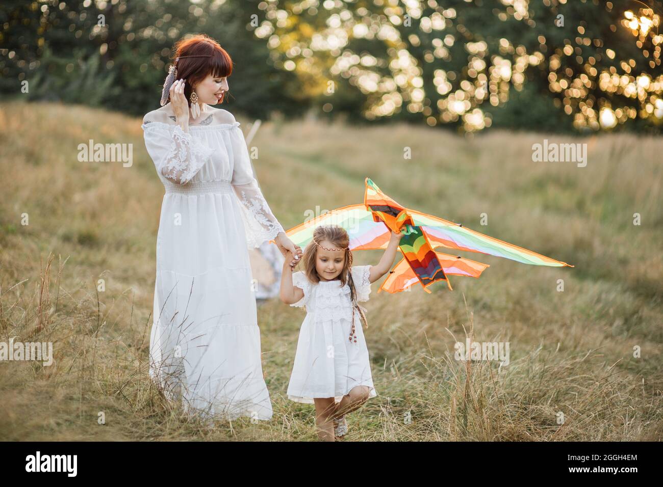 Glückliche Familie, Urlaub, Muttertagskonzept. Charmante Mutter und ihre niedliche, entzückende kleine Tochter, die bei Sonnenuntergang einen Drachen über die Natur startend. Boho Hippie Mama und Kind spielen mit Drachen auf dem Feld Stockfoto