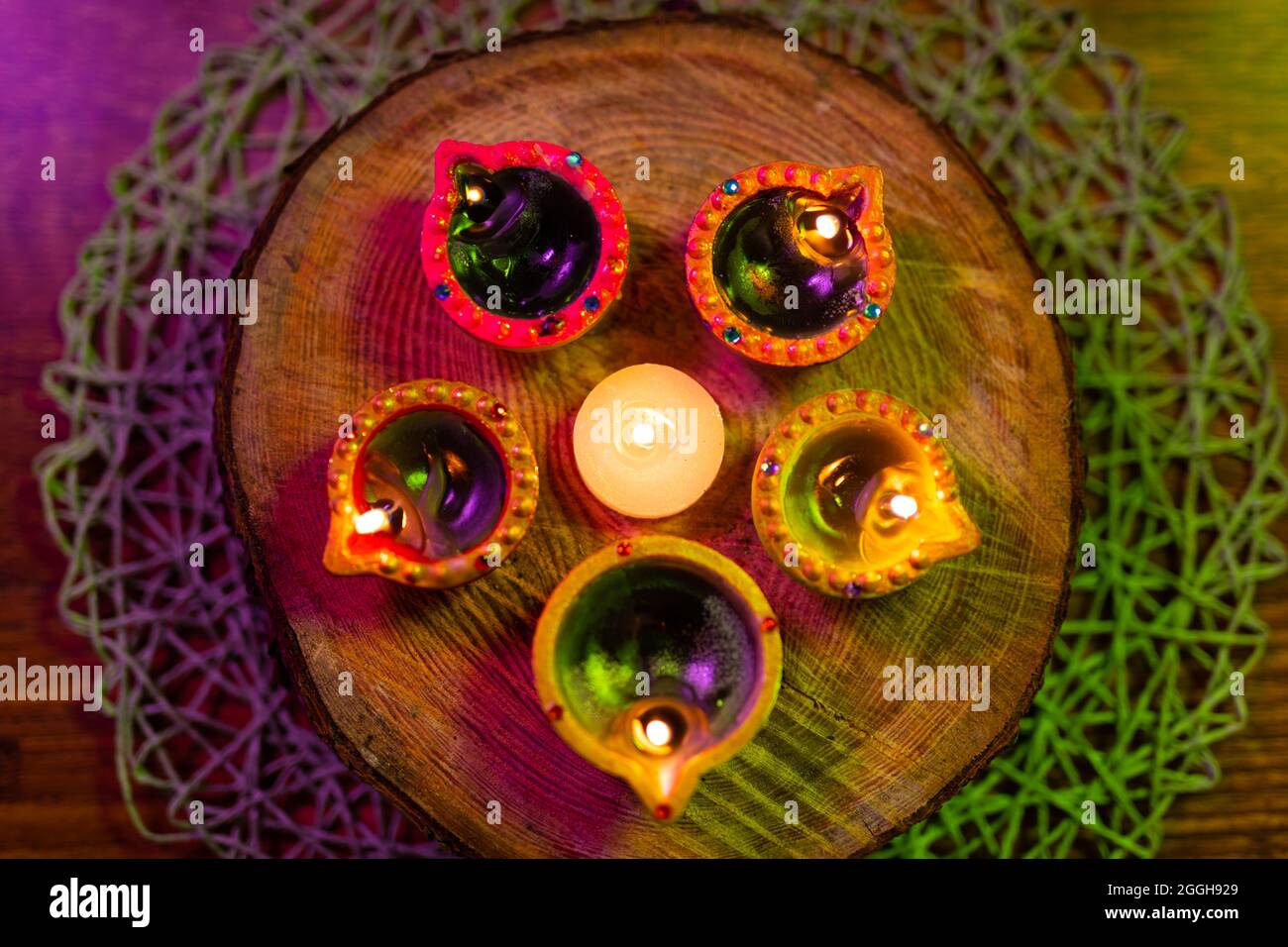 Vier brennende Kerzen in kleinen dekorativen Tontöpfen und Teelicht-Kerze, die auf einem runden Holzbrett brennt Stockfoto