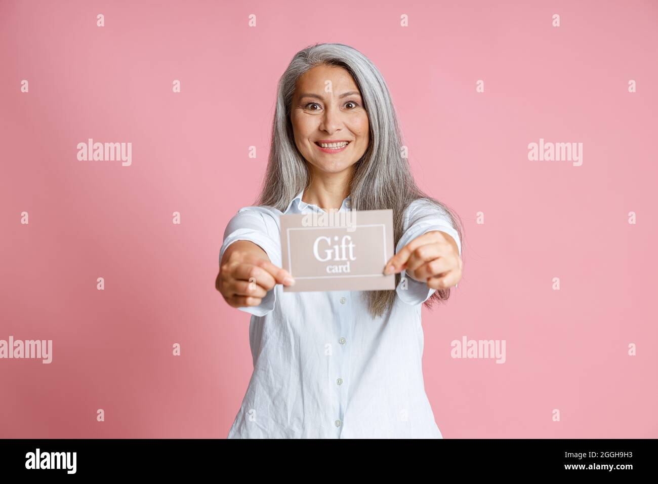 Attraktive grauhaarige asiatische Dame hält Geschenkkarte auf rosa Hintergrund Stockfoto