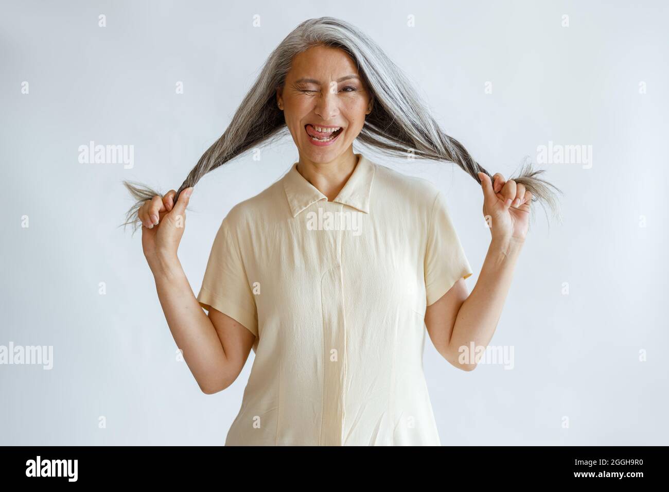 Asiatische Dame mittleren Alters frattert und hält lange silberne Haare auf hellgrauem Hintergrund Stockfoto