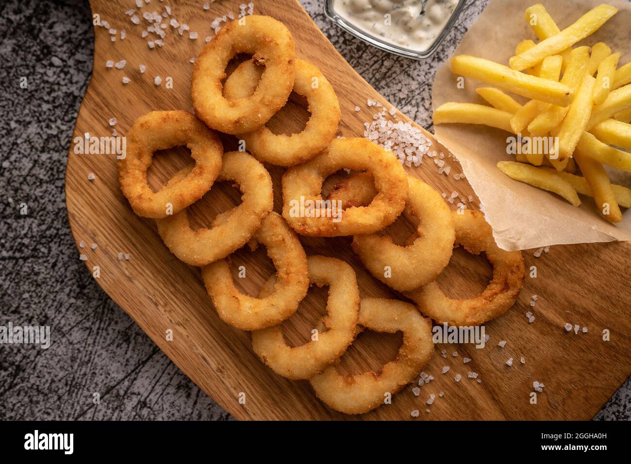 Selektiver Fokus. Gebratene Zwiebelringe in Semmelbröseln, in Öl gebraten. Mit natürlicher Sauce. Restaurant-Servieren. Auf dunklem Hintergrund. Für Menüs und Werbung Stockfoto