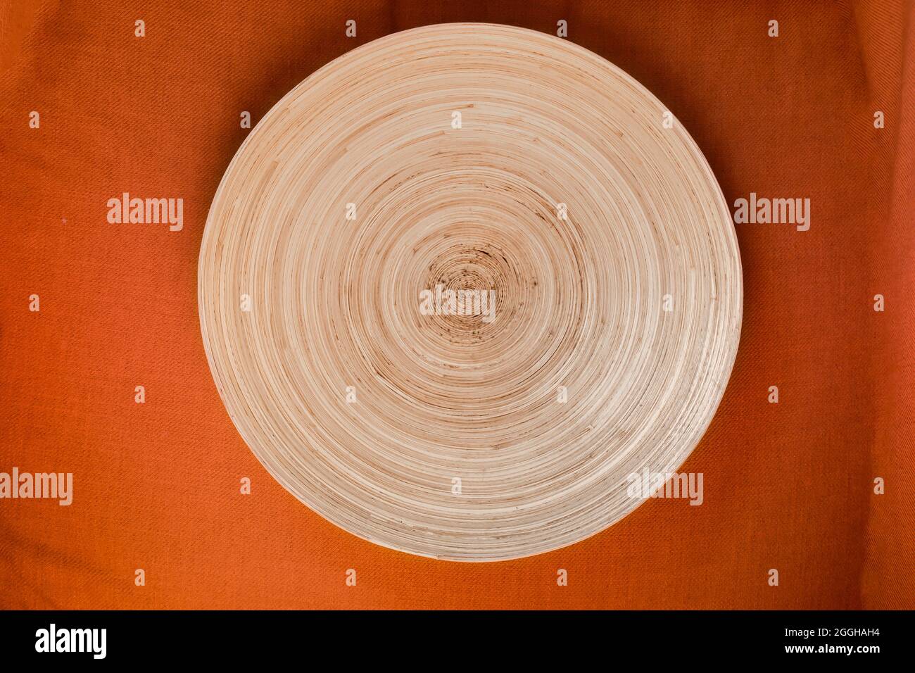 Handgefertigtes dekoratives rundes Tablett aus Pflanzenfasern auf orangefarbenem Tischlorh Draufsicht Stockfoto