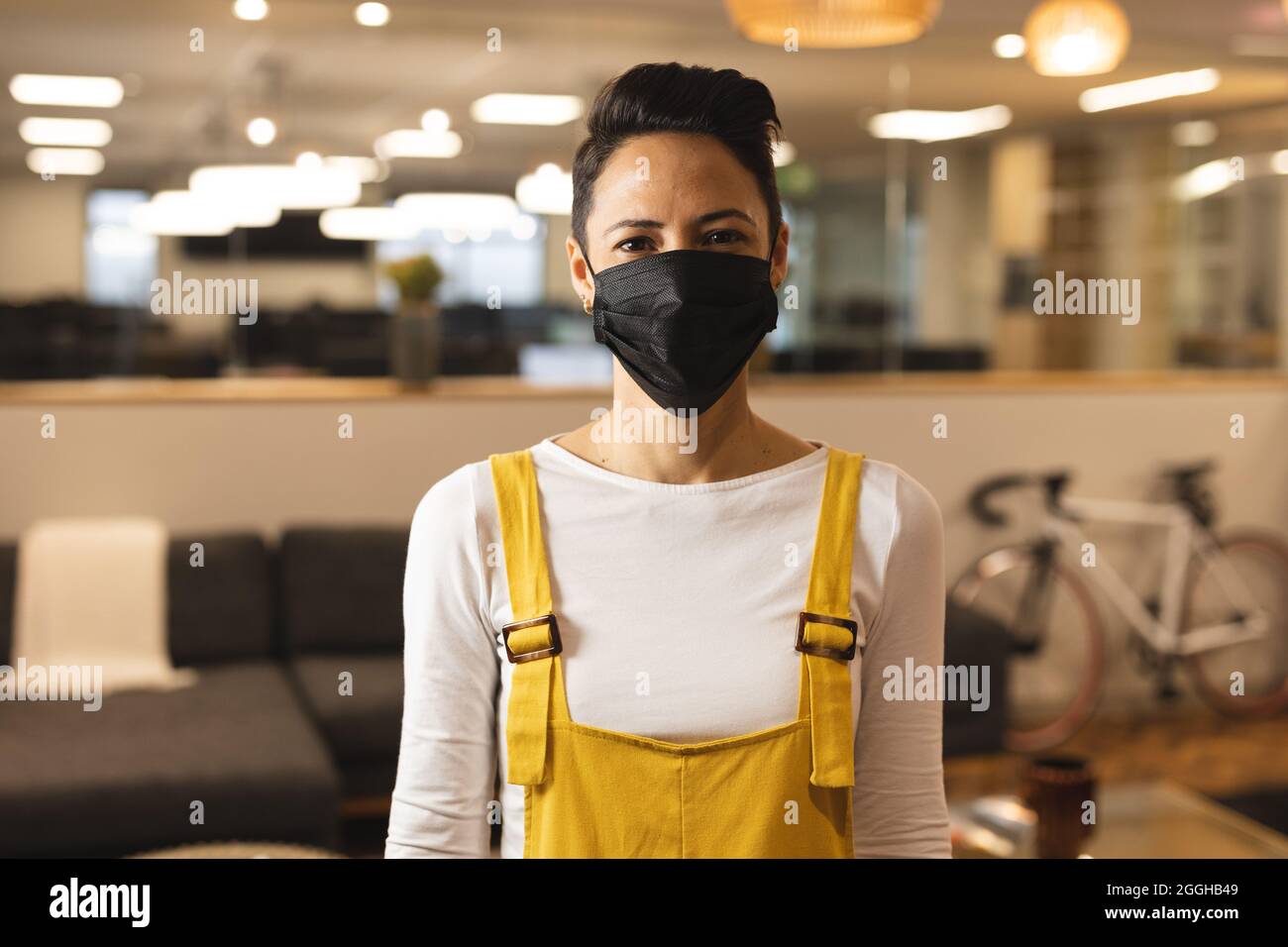 Portrait einer Mischtrassengestalt Frau, die Gesichtsmaske trägt, bei der Arbeit, mit Blick auf die Kamera Stockfoto