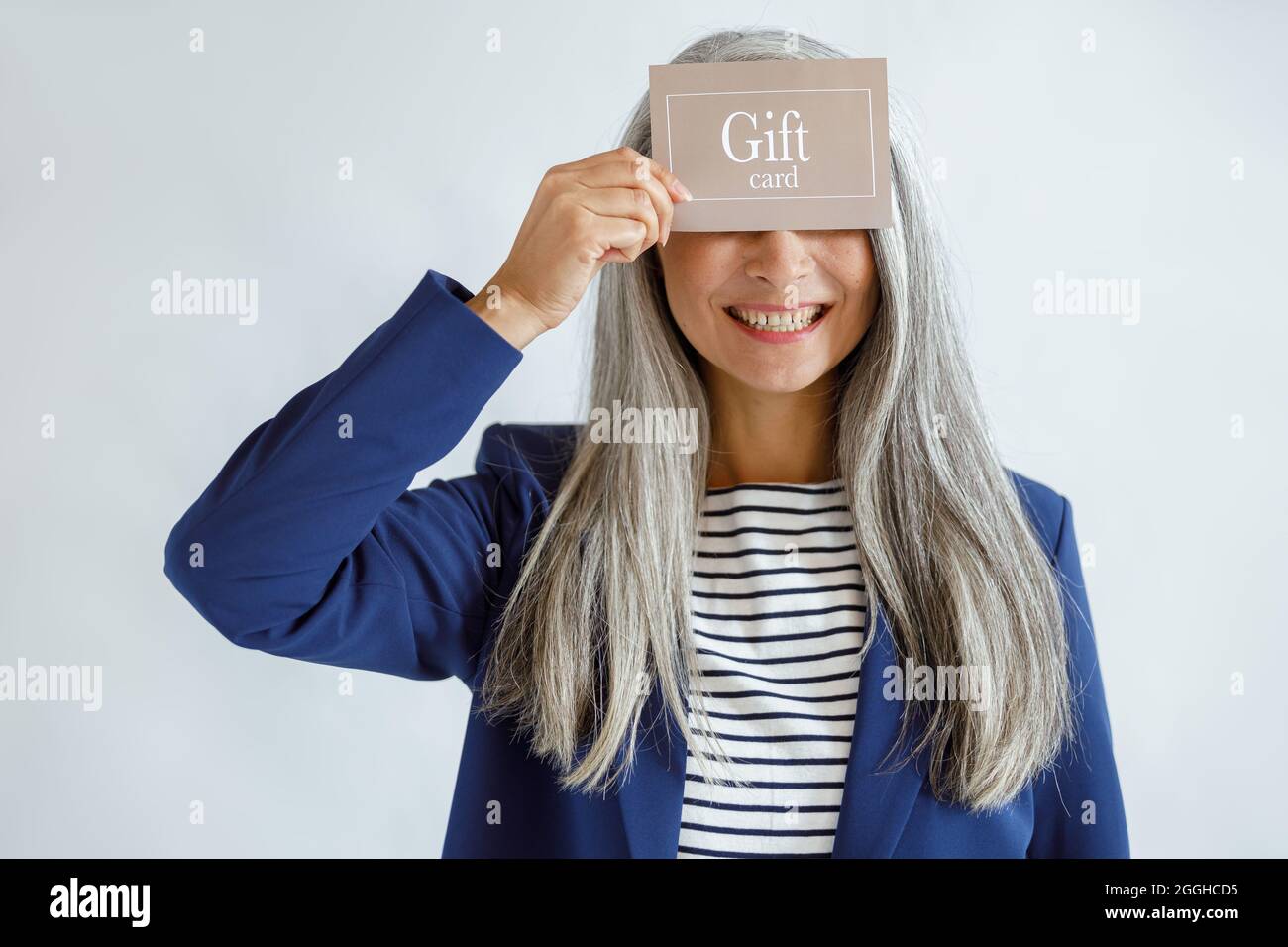 Lächelnde reife Dame mit lockeren Haaren hält Geschenkkarte auf hellgrauem Hintergrund Stockfoto