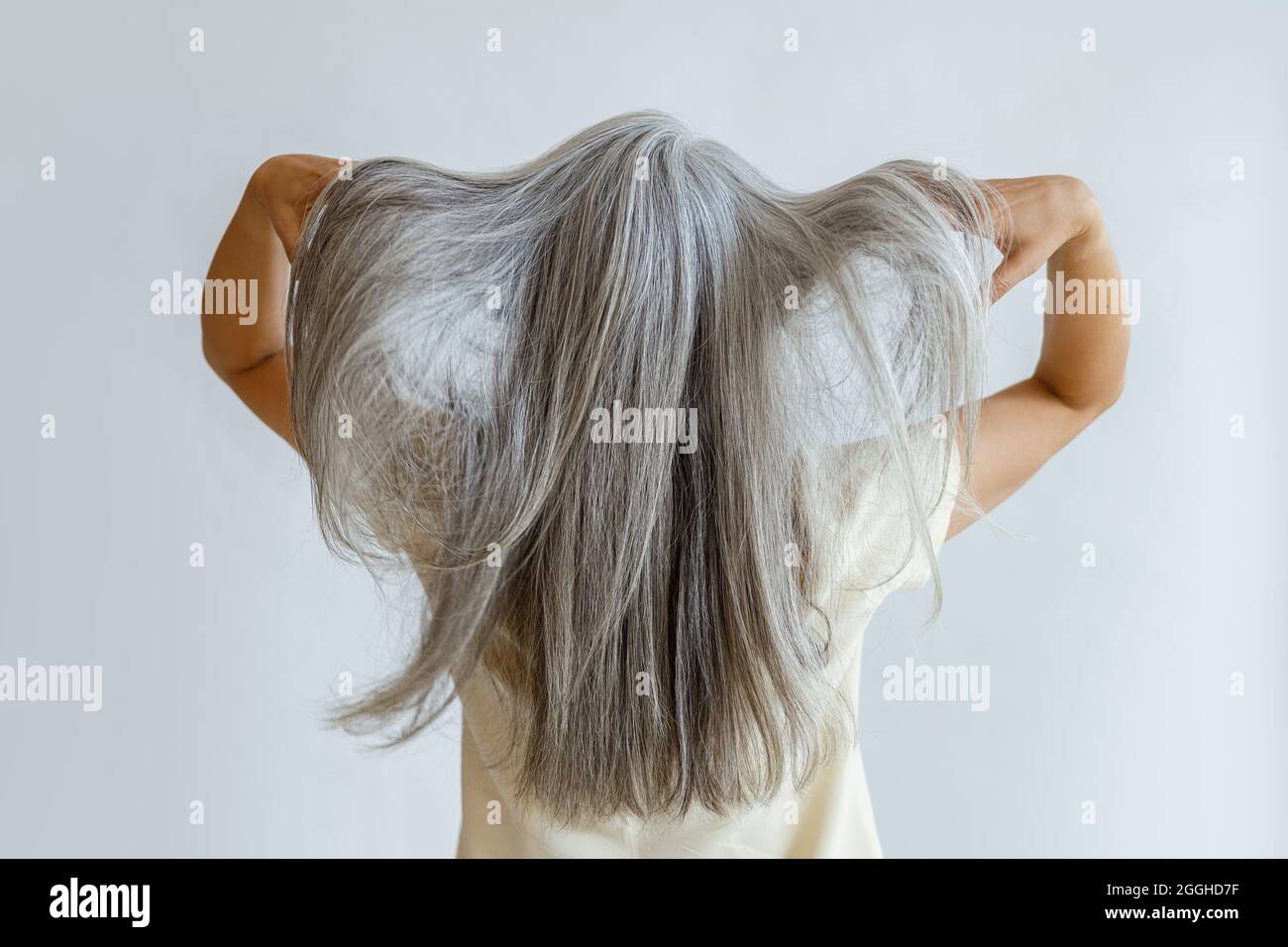 Frau mittleren Alters zeigt lange lose graue Haare stehen auf hellem Hintergrund Stockfoto