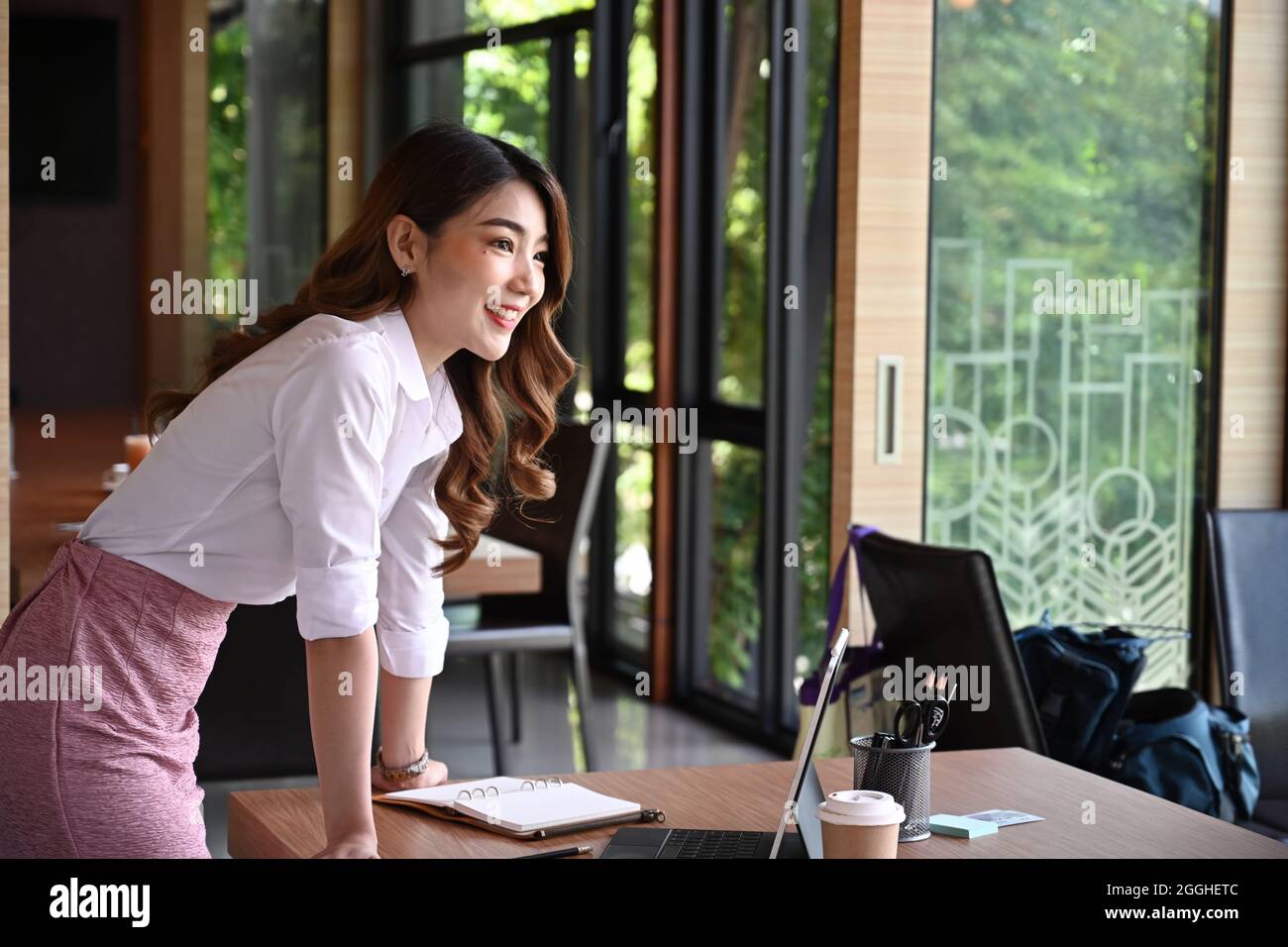 Attraktive asiatische Geschäftsfrau, die im Büro steht und aus dem Fenster schaut. Stockfoto