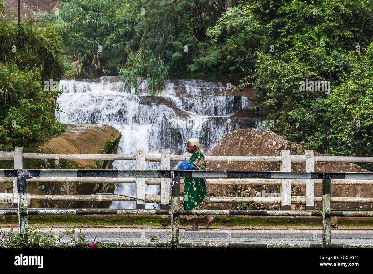 Alte Frau, die vor dem Ramboda Wasserfall, Nuwara Eliya, Sri Lanka, läuft Stockfoto