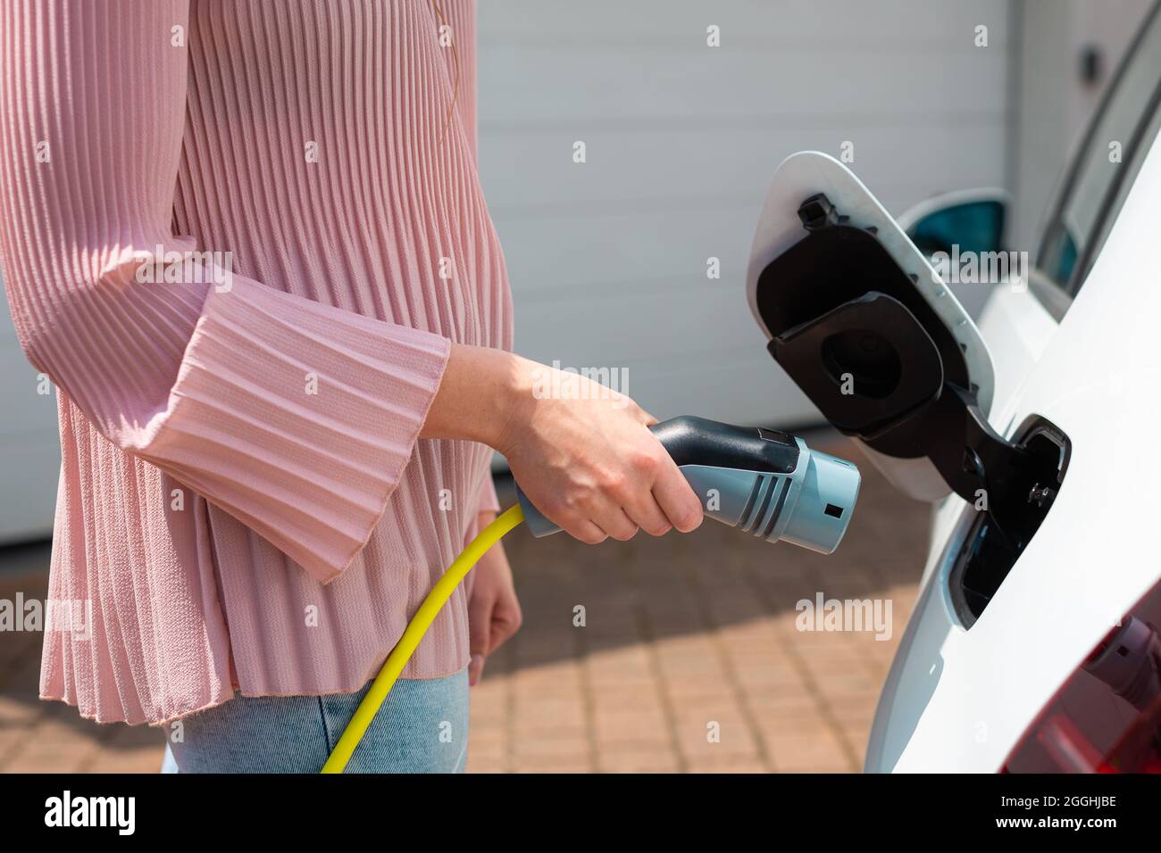 Frau, die einen Ladestecker oder ein Ladegerät in ein weißes Elektroauto steckt Stockfoto