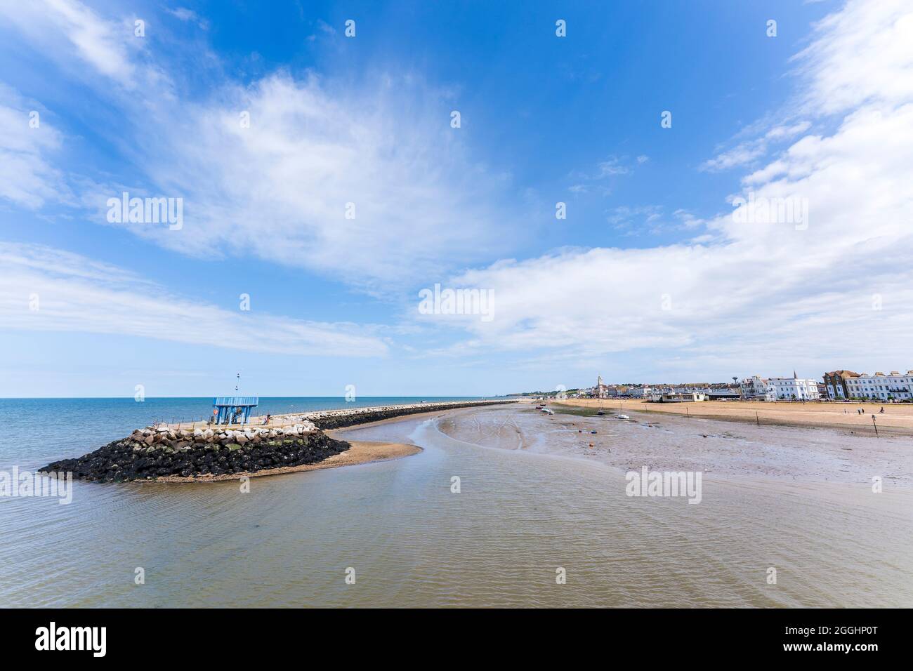 Weitwinkelansicht der Strandpromenade von Herne Bay mit dem Uhrenturm und dem einzigen Pier-Hafen bei Ebbe an einem Sommertag mit blauem Himmel und weißen Wolken. Stockfoto