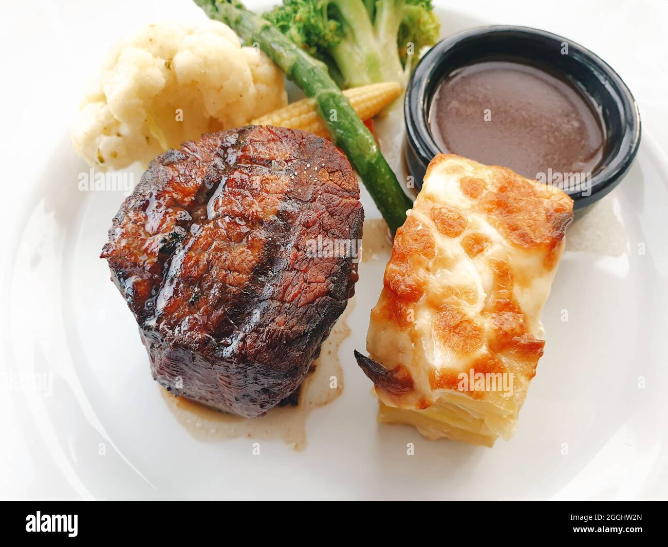 Köstliches Steak Filet Mignon serviert mit Sauce, Babykorn, Gebäck, Brokkoli, Blumenkohl und Spargel auf einem Teller im Restaurant. Stockfoto