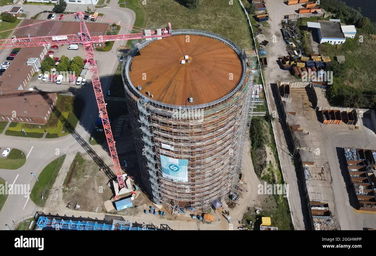 Rostock, Deutschland. September 2021. Das Richtfest für den neuen Wärmespeicher der Stadtwerke Rostock findet statt. Der Grundstein für das 55 Meter hohe Bauwerk am Warnow River wurde vor eineinhalb Jahren gelegt, die Inbetriebnahme ist für das Frühjahr 2022 geplant. Der drucklose Stahltank speichert 45 Millionen Liter Wasser bei einer Temperatur von 98 Grad Celsius und führt es bei Bedarf in das Heiznetz ein. Das Reservoir wird unter anderem helfen, Energie aus Wind- und Solarkraftwerken zu speichern. (Luftaufnahme mit Drohne/Kopter) Quelle: Bern/dpa/Alamy Live News Stockfoto