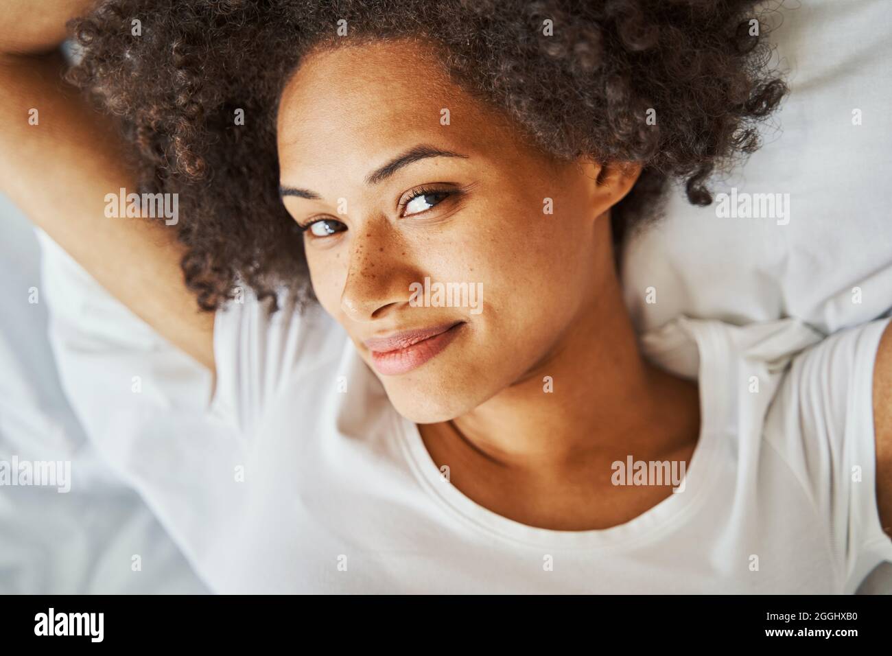 Weibchen mit lockigen Haaren, die die Zeit im Bett verflüchtigen Stockfoto