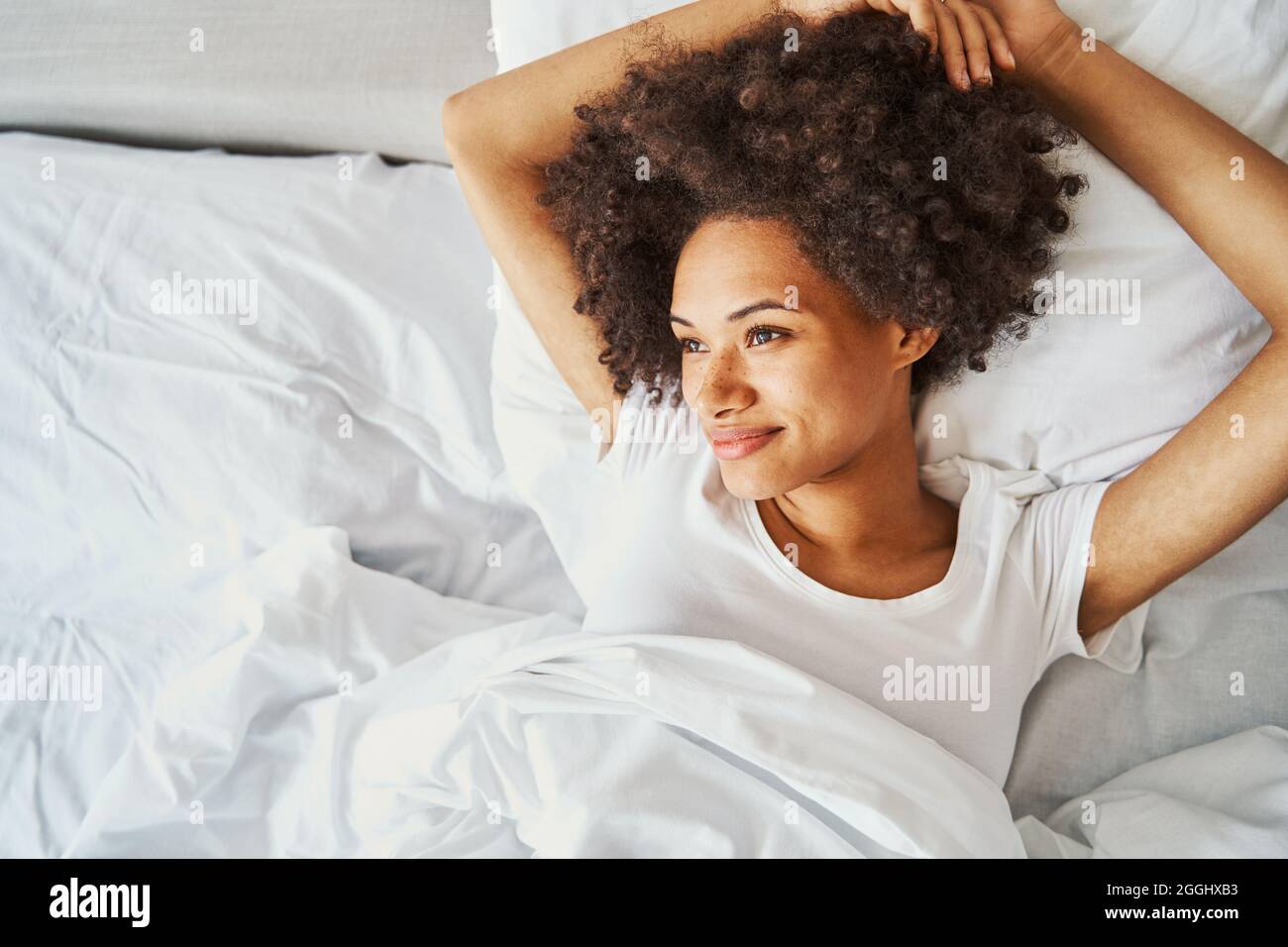 Heitere niedliche lockige Dame, die im Bett träumt Stockfoto