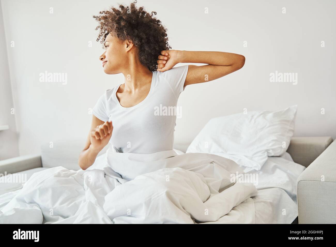 Eine gelassene, lockige Dame streckte ihre Arme nach dem Schlaf Stockfoto