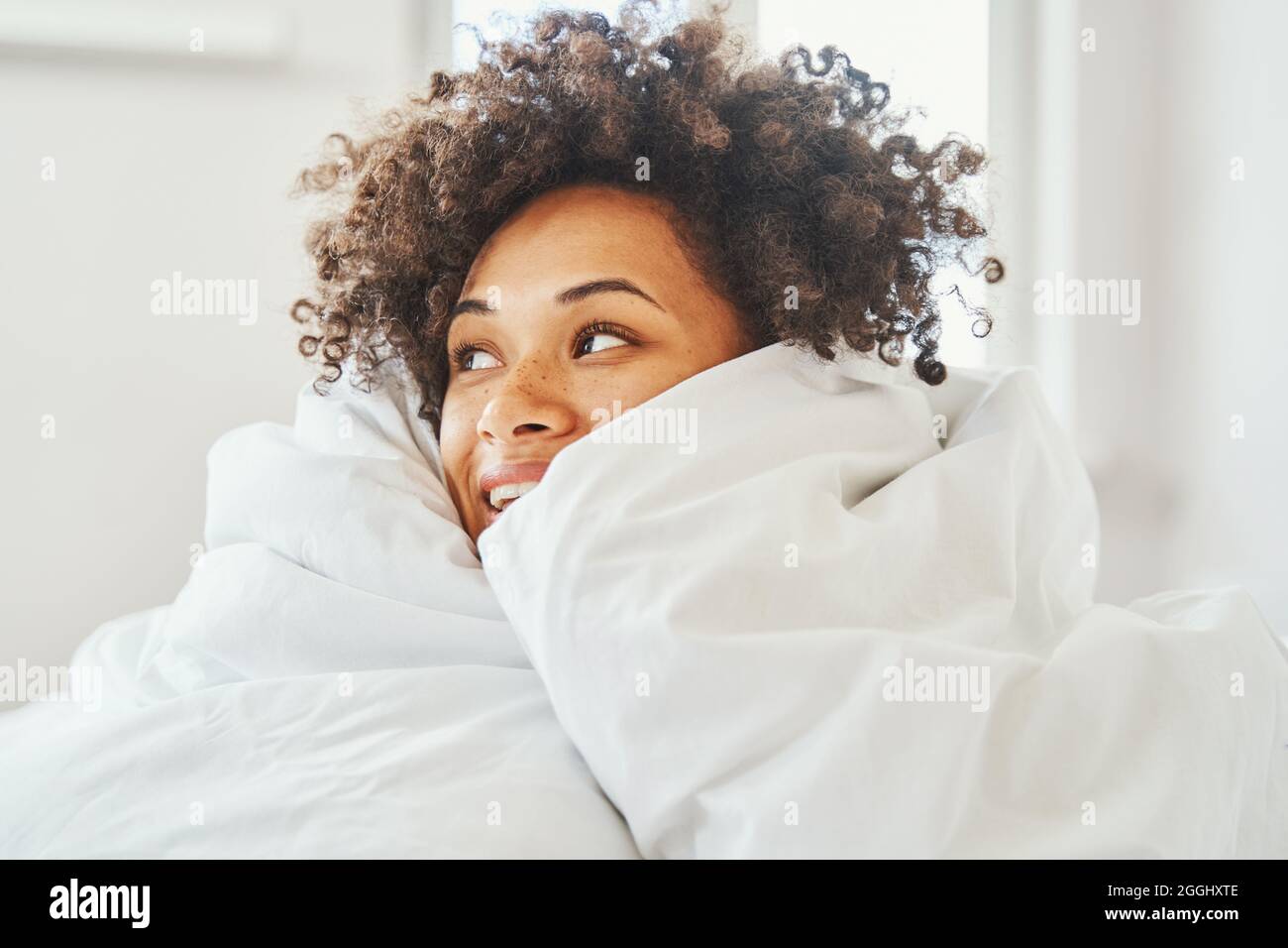 Freudig lockig-haarige attraktive weibliche Tagträumerin im Bett Stockfoto