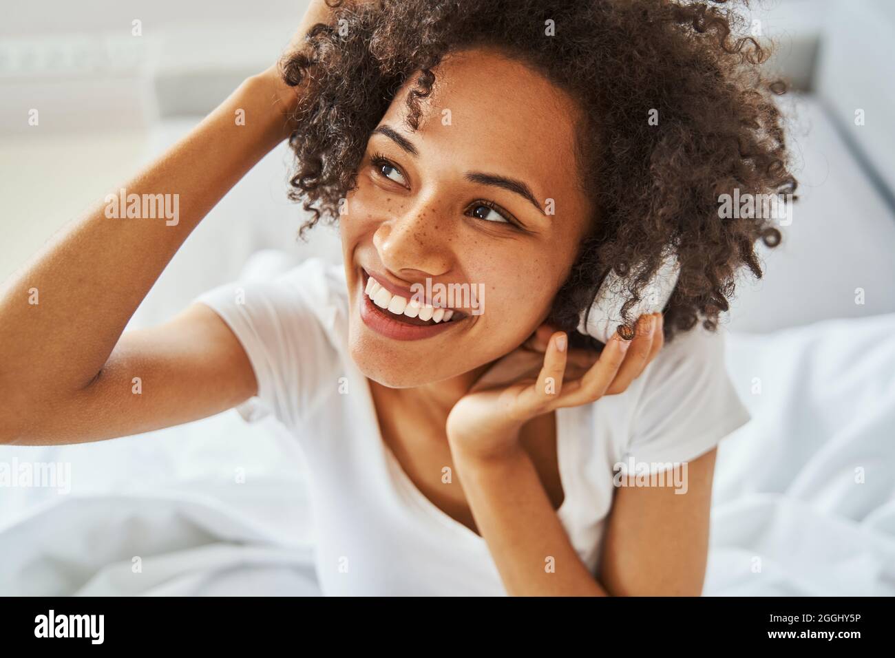 Fröhliche, hübsche Dame in kabellosen Kopfhörern schaut weg Stockfoto