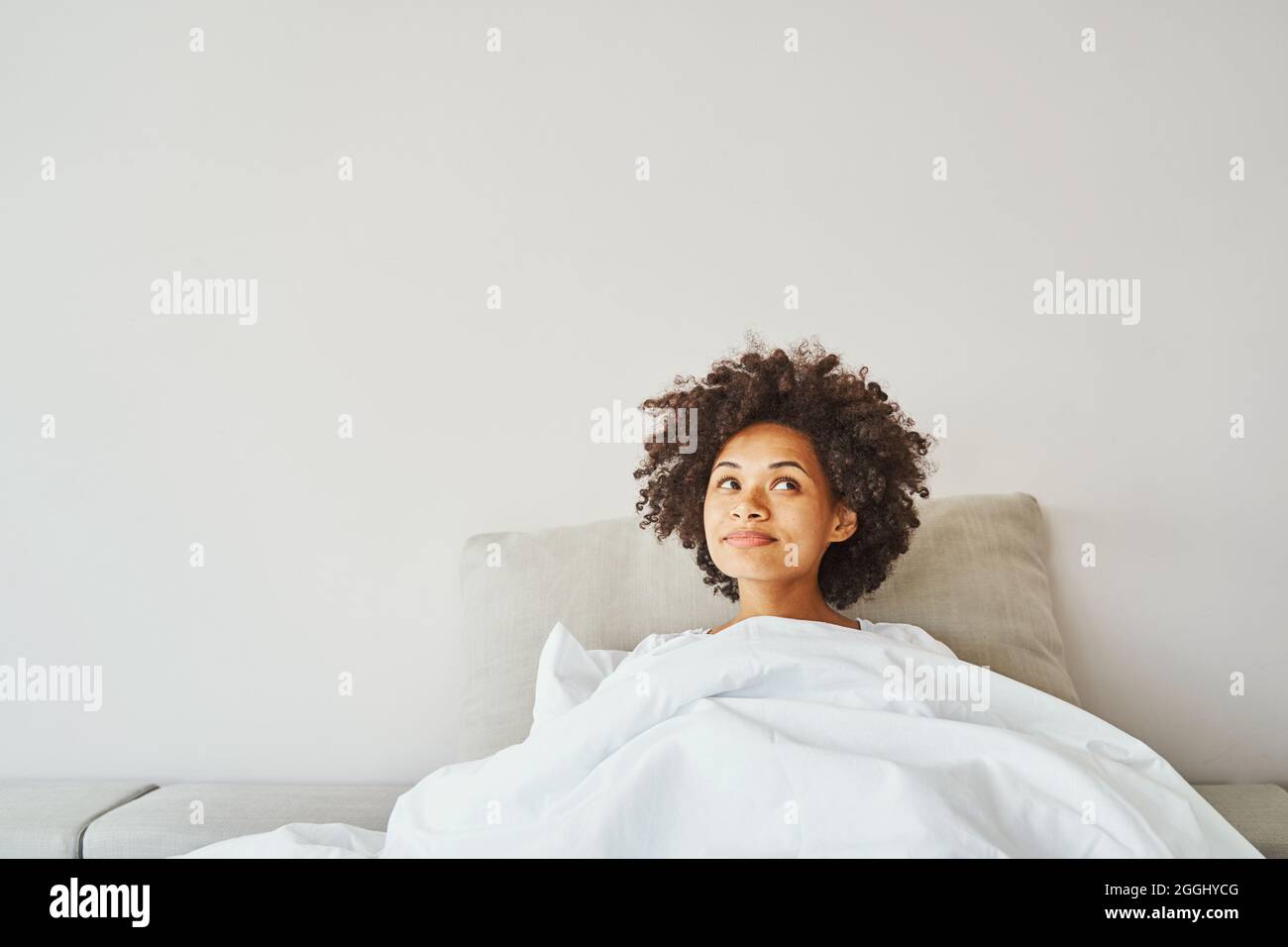 Porträt einer verträumten, zufriedenen afroamerikanischen Frau mit dunklem lockigen Haar, das im Bett liegt Stockfoto